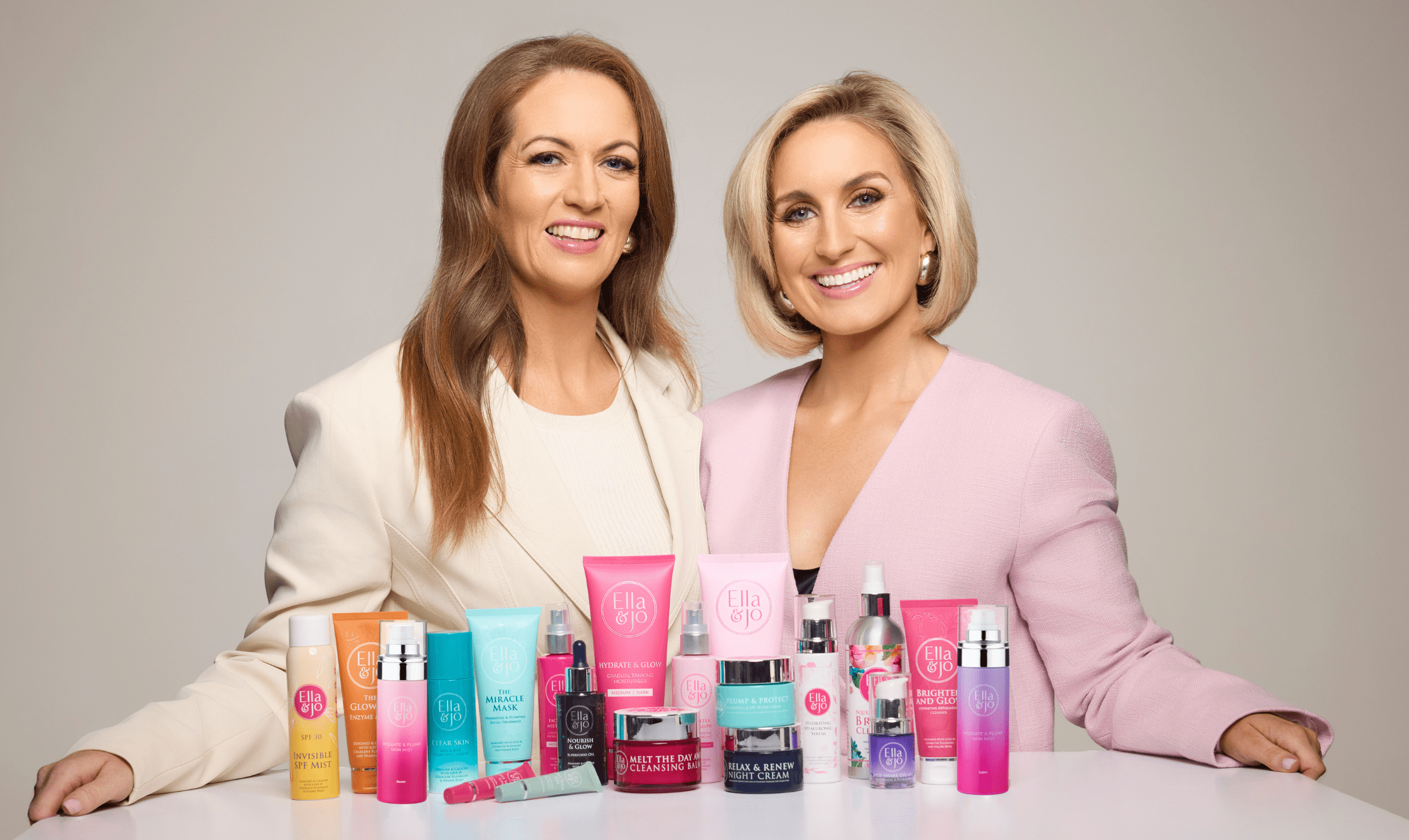 Niamh and Charlene standing behind a table with skincare products on a neutral background